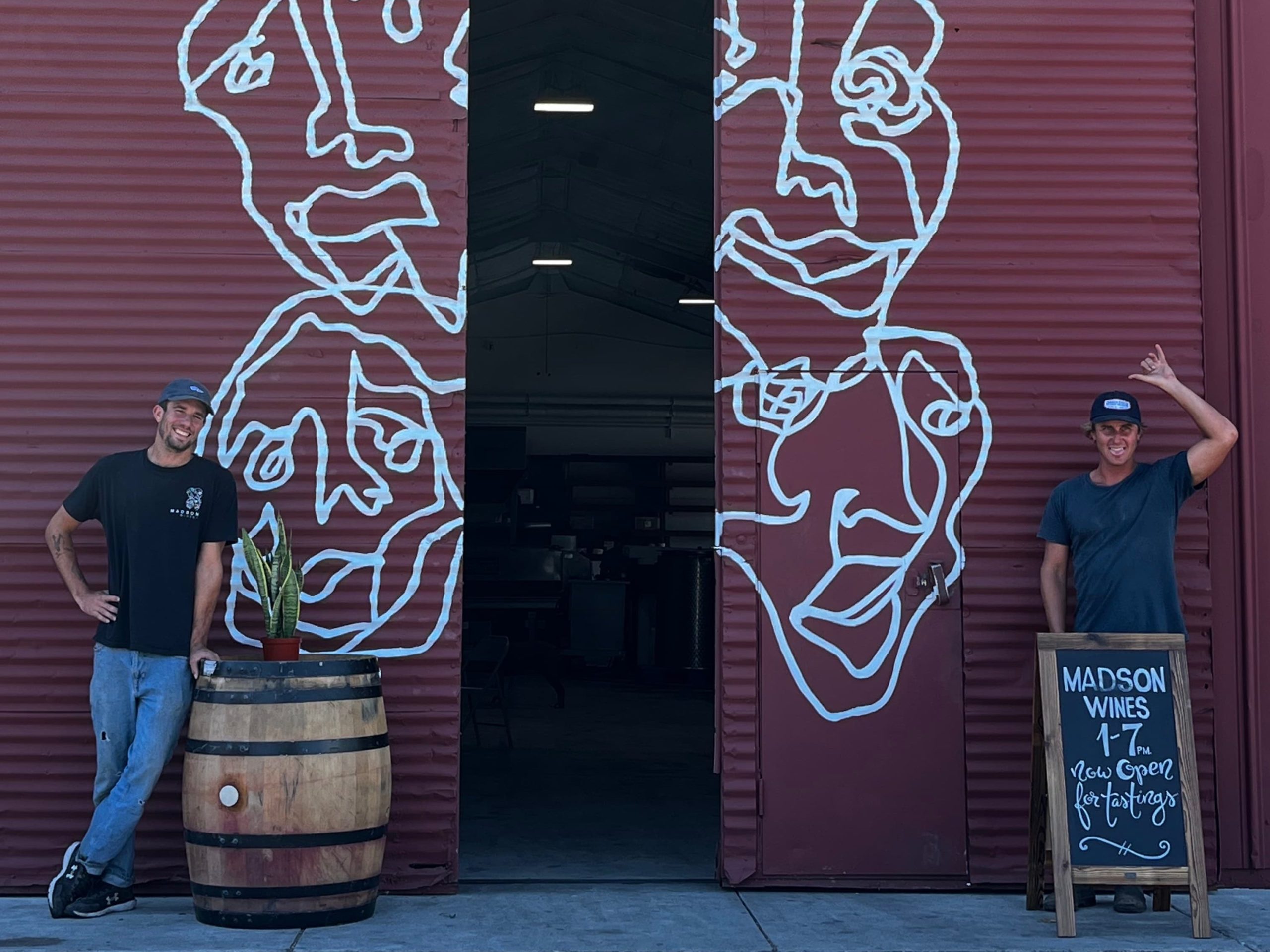 Cole and Tino are standing outside the tall, barn-style door of the Madson tasting room